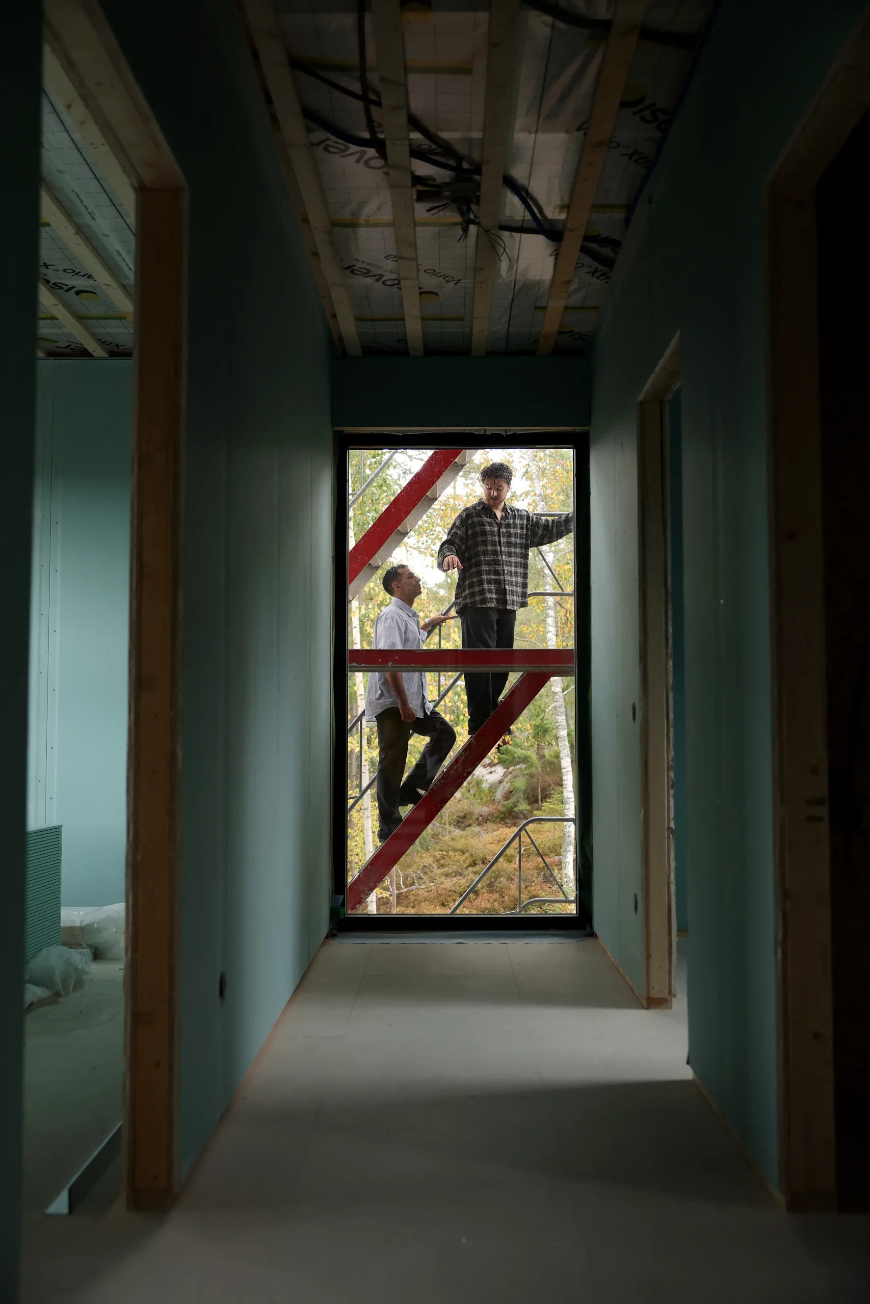 Två medarbetare på byggnadsställningen sedda genom en dörröppning i ett hus under uppförande